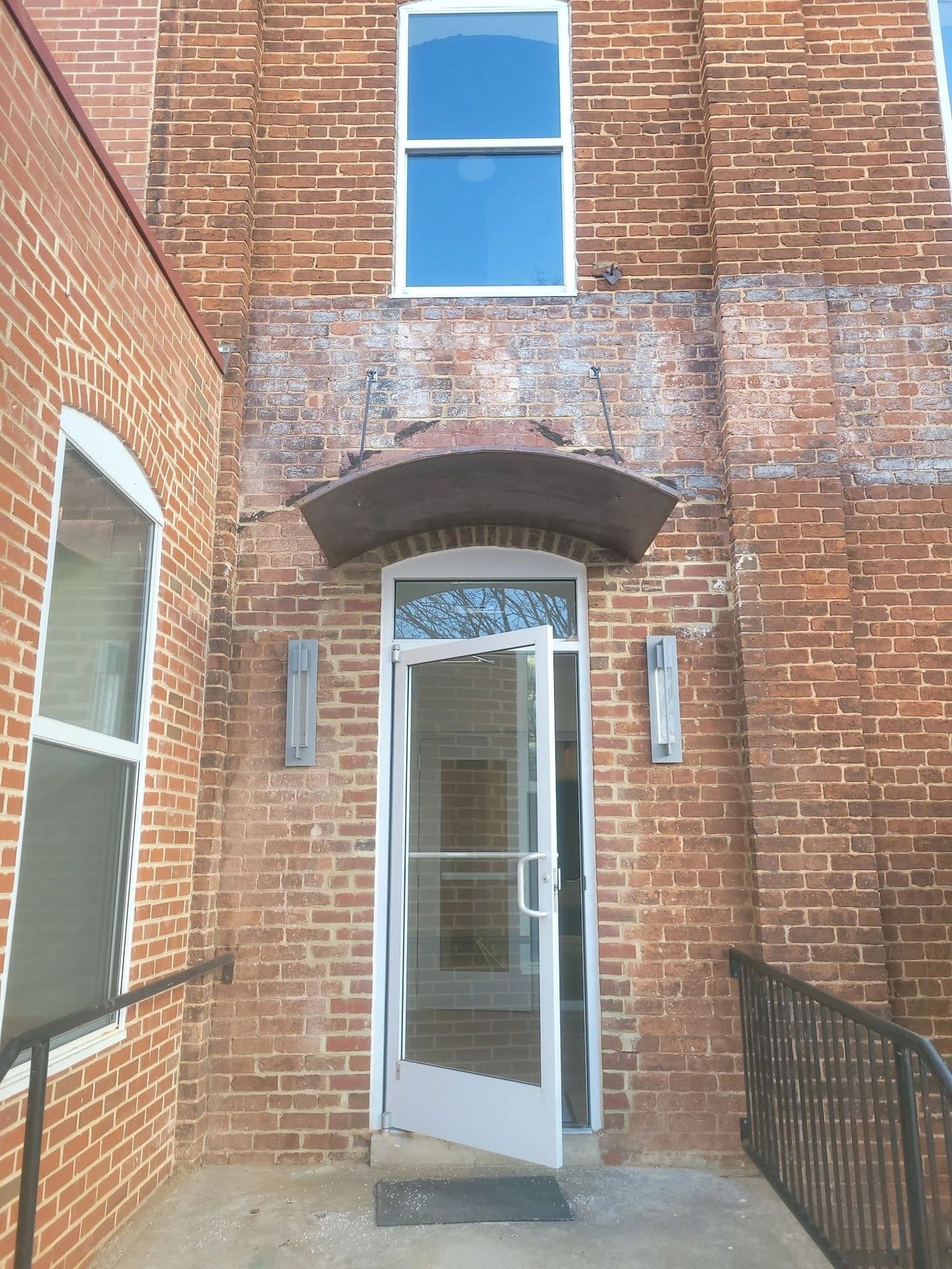 Open glass door on a red brick building with a window above.