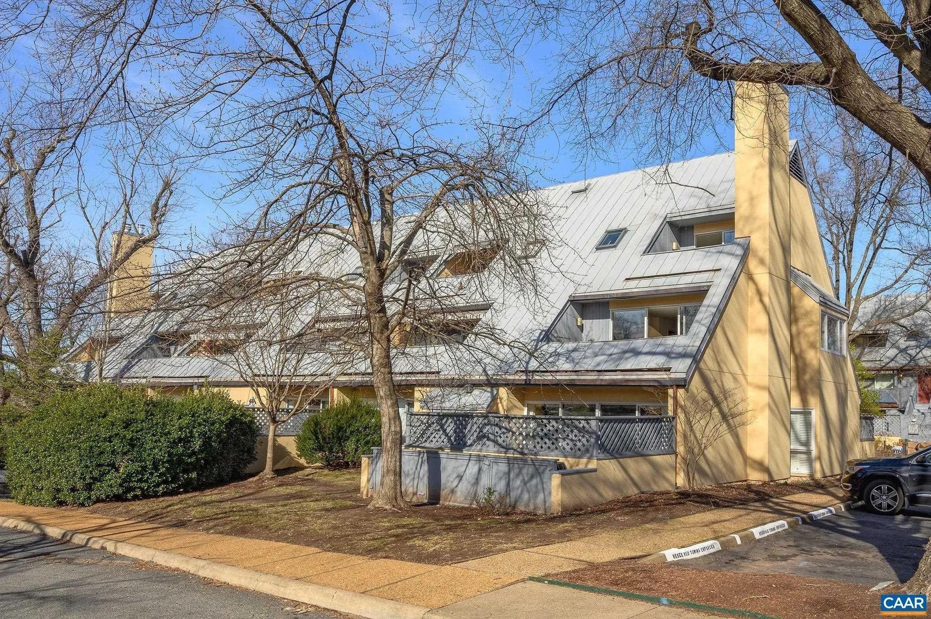 Unique angled roof residential building with large chimneys and leafless trees.