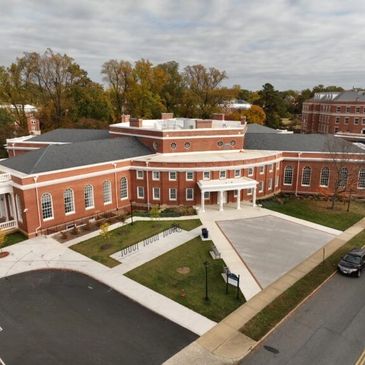 A large red brick building with white columns and multiple windows surrounded by greenery.